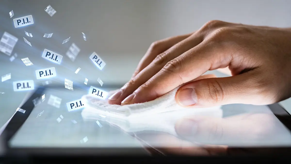 A hand wiping a tablet screen to remove PII data fragments representing digital privacy and data protection.