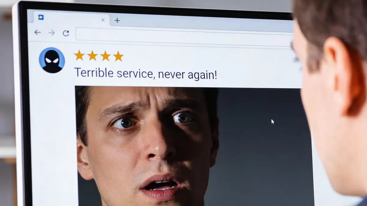 A man staring at a computer screen displaying a negative review with a four-star rating.