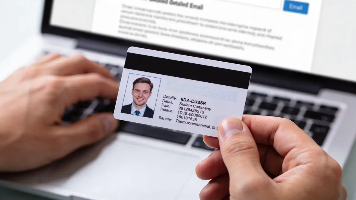 A person holding an identification card while typing on a laptop computer in an office setting.