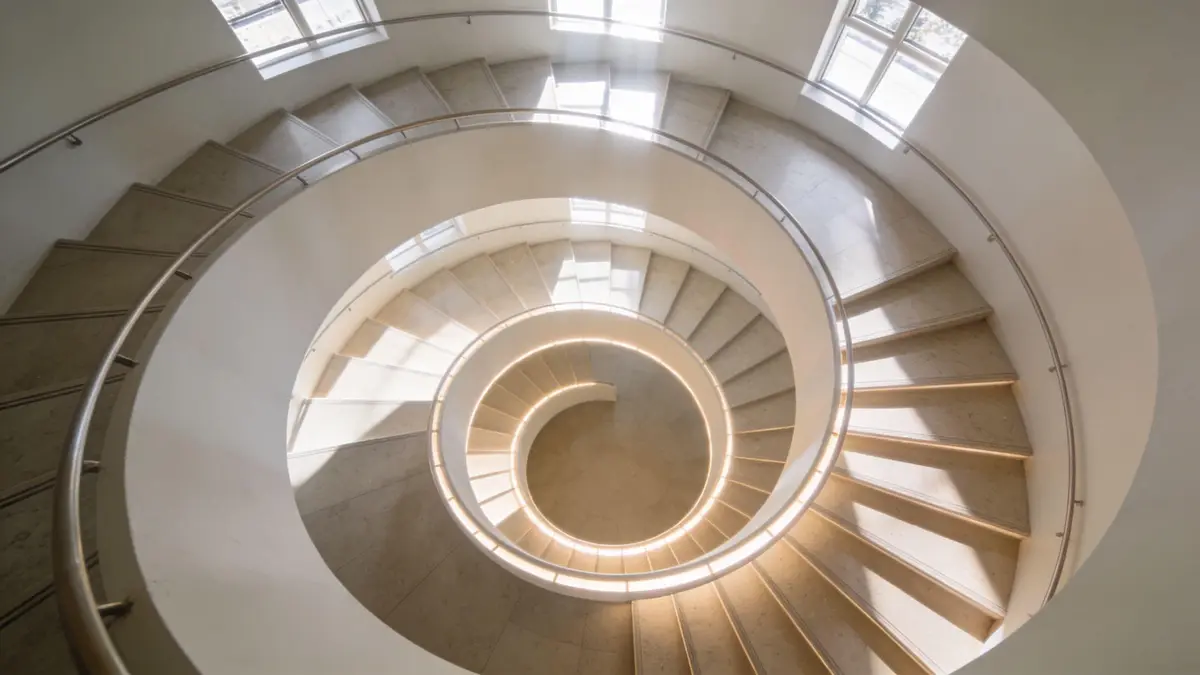 A top-down view of a bright, modern spiral staircase with stone steps and integrated lighting.